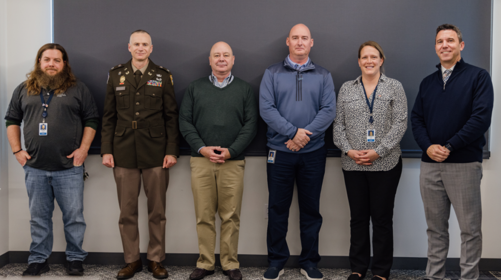 League staff veterans were honored at the November League of Minnesota Cities Board of Directors meeting. Six of the eight veterans are shown leaning against a wall in the office.