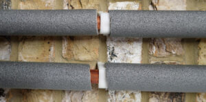 Three copper water pipes against a brick wall in grey foam insulation