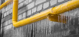 A yellow icy pipe with gas on the background of a gray wall