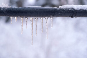 Frozen icicles on a gray pipe after a thaw in winter